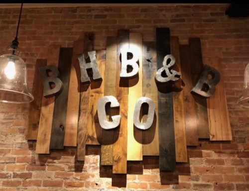 Wooden wall art featuring the letters "B H B & B G O" against a brick background.