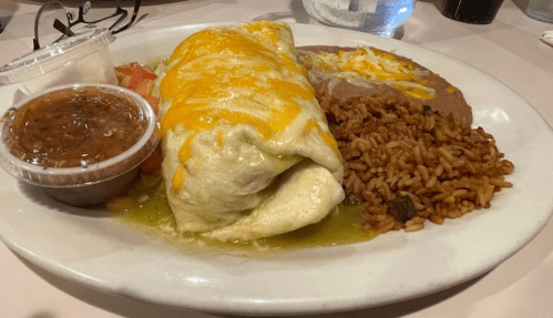 A plate of a large burrito topped with cheese, served with rice, refried beans, and salsa on the side.