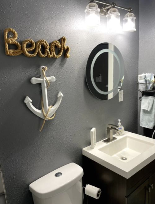 A modern bathroom featuring a nautical theme with an anchor, "Beach" decor, and a sleek sink and mirror.