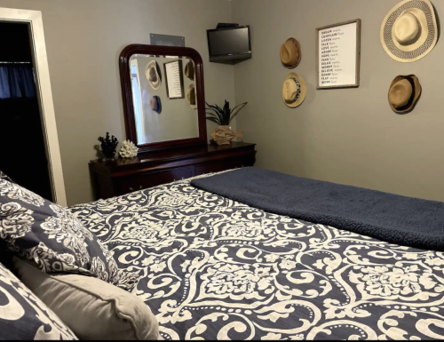 Cozy bedroom featuring a patterned bedspread, a mirror, a dresser, and decorative hats on the wall.