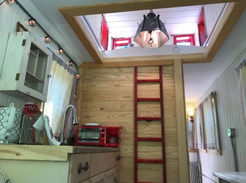 Cozy interior of a tiny home featuring a wooden ladder, red accents, and a bright skylight.