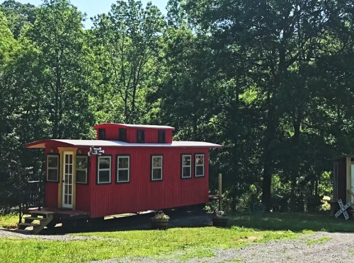 A bright red caboose-style tiny house surrounded by lush green trees.