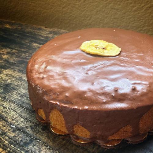 A round chocolate cake topped with a slice of dried banana, resting on a wooden surface.