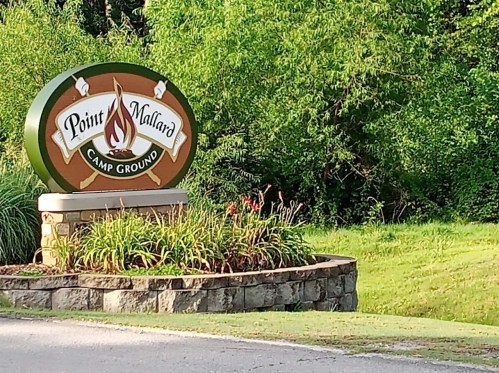 Sign for Point Mallard Camp Ground surrounded by greenery and flowers.