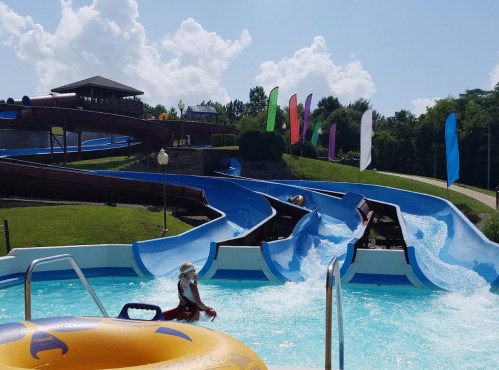 A water park scene featuring colorful slides, a pool, and a sunny sky with fluffy clouds.