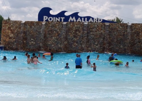 A group of people enjoying a water park with a stone wall and "Point Mallard" sign in the background.