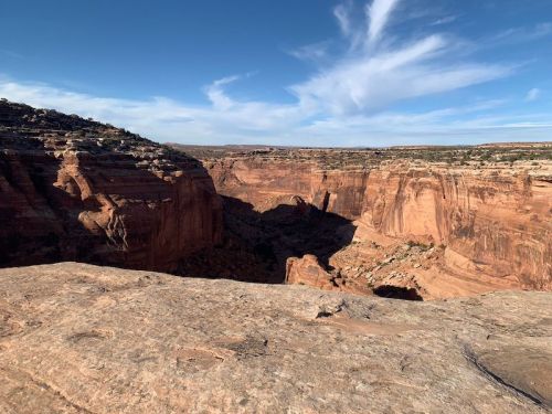 A vast canyon landscape with red rock formations under a clear blue sky and wispy clouds.