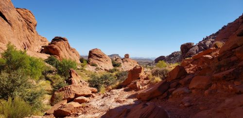 A scenic view of red rock formations and desert vegetation under a clear blue sky.