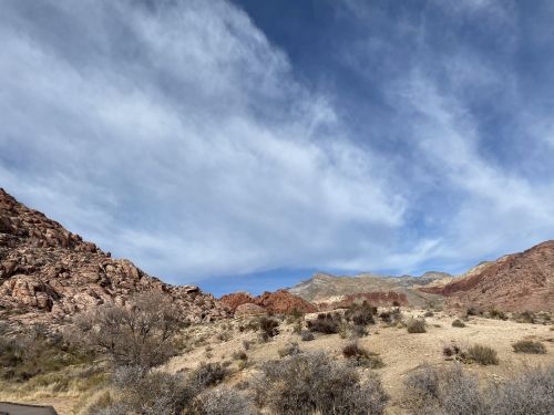 A scenic view of rocky hills under a blue sky with wispy clouds, featuring dry grass and sparse vegetation.
