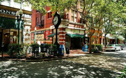 A charming street scene with shops, a clock, and trees casting dappled shadows on the sidewalk.