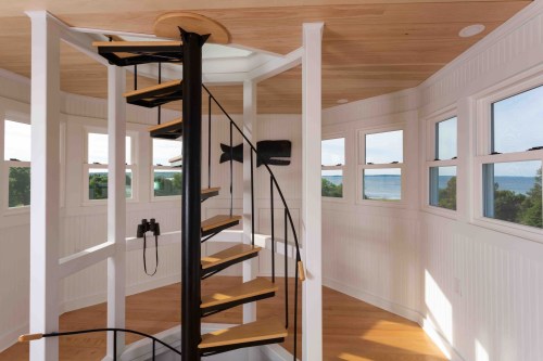 A spiral staircase in a bright, airy room with large windows overlooking a scenic view.