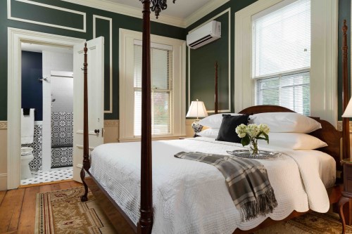 Cozy bedroom with a dark green wall, a large bed, and an adjoining bathroom visible through an open door.