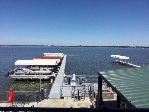 A serene lake view with docks and boats under a clear blue sky, featuring outdoor seating and a red umbrella.
