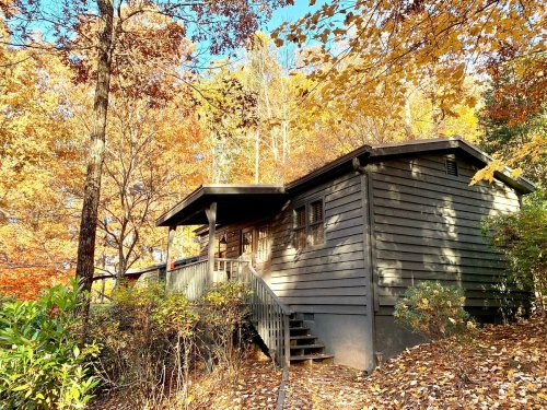 A cozy wooden cabin surrounded by vibrant autumn foliage and colorful trees.