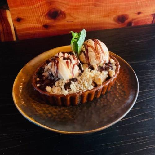 A dessert bowl with two scoops of ice cream, chocolate drizzle, and crumbled toppings, garnished with a mint leaf.