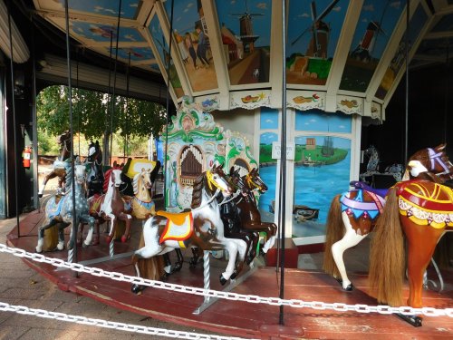 A colorful carousel with intricately painted horses and a scenic backdrop, surrounded by a chain barrier.