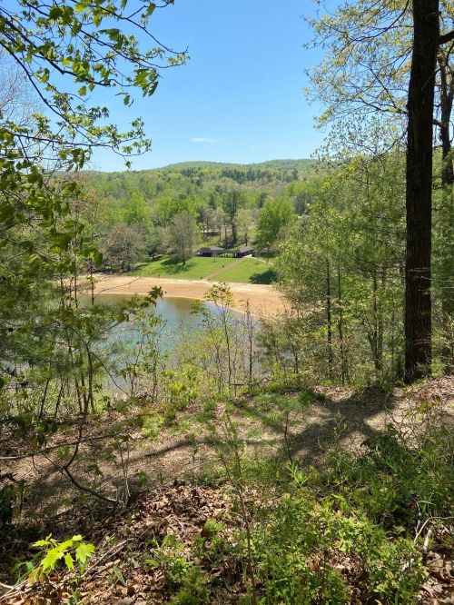 A scenic view of a lake surrounded by green trees and rolling hills under a clear blue sky.