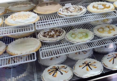A display case filled with various pies, including cream and fruit varieties, each labeled with names.
