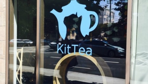 Window display of KitTea featuring a teapot logo and a circular design, with a street view in the background.