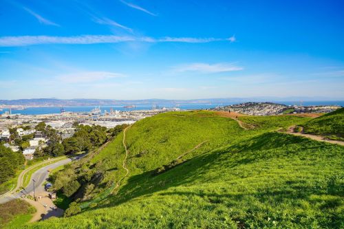 A scenic view of green hills overlooking a bay and cityscape under a clear blue sky.