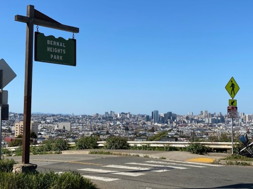 Sign for Bernal Heights Park with a city skyline in the background on a clear day.