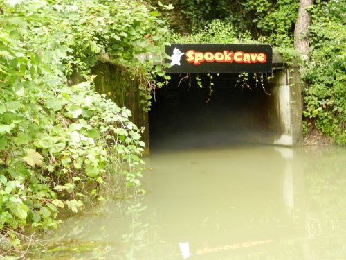 A dark tunnel entrance labeled "Spook Cave," surrounded by lush greenery and murky water.