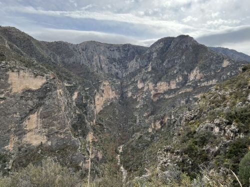 A scenic view of rugged mountains and cliffs under a cloudy sky, showcasing a deep valley between the peaks.