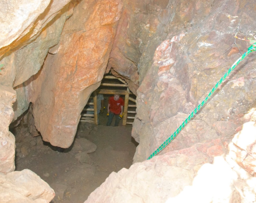A person in a red shirt stands inside a rocky cave, with wooden supports visible in the background.