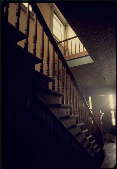 A dimly lit staircase with wooden banisters leading to an upper level, featuring a window at the top.