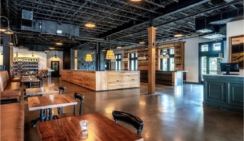Modern restaurant interior featuring wooden tables, leather seating, and a spacious bar area with warm lighting.
