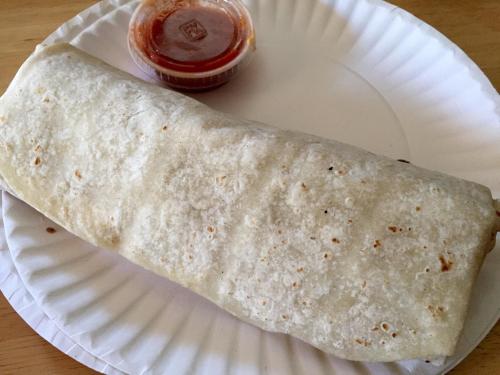 A large burrito on a paper plate, accompanied by a small container of red salsa.