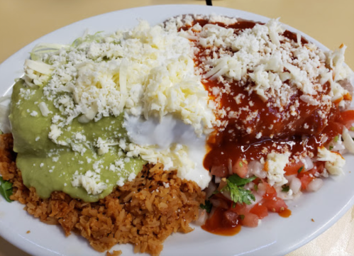 A plate of rice topped with green and red sauces, sour cream, diced tomatoes, and shredded cheese.