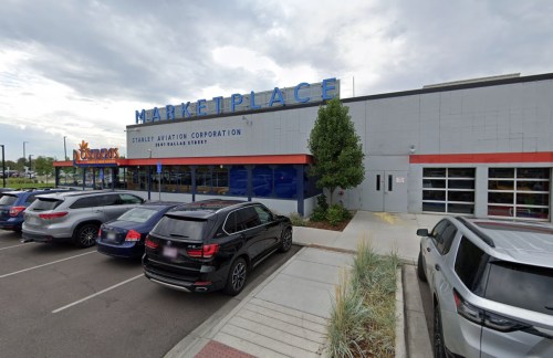 Exterior view of a building labeled "Marketplace" with parked cars in front and a cloudy sky above.