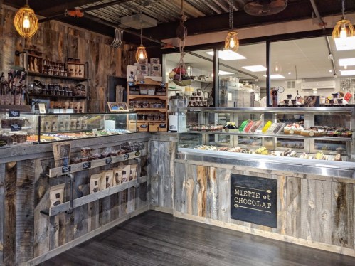 A cozy chocolate shop interior with wooden decor, showcasing various chocolates and confections in glass displays.