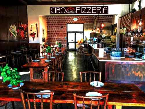 Interior of Cibo Pizzeria featuring wooden tables, a bar, and a warm, inviting atmosphere.