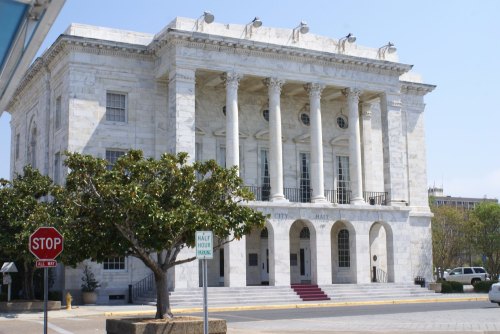 Historic building with large columns, a white facade, and a tree in front, set against a clear blue sky.