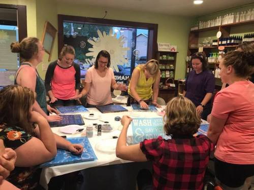 A group of women engaged in a crafting activity at a workshop, creating designs on fabric at a well-lit store.