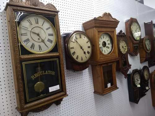 A collection of vintage wall clocks in various styles and sizes displayed on a white pegboard background.