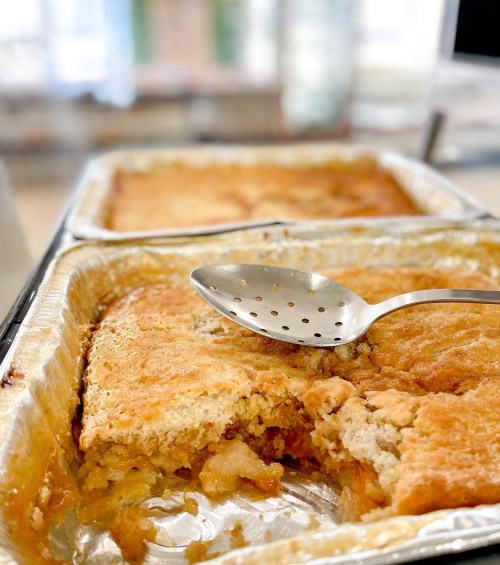 A close-up of a baked dessert in a foil pan, with a spoon resting on top and a portion cut out.