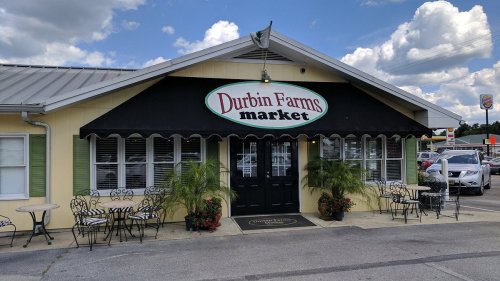 Exterior of Durbin Farms Market, featuring a yellow building, black awning, and outdoor seating with potted plants.