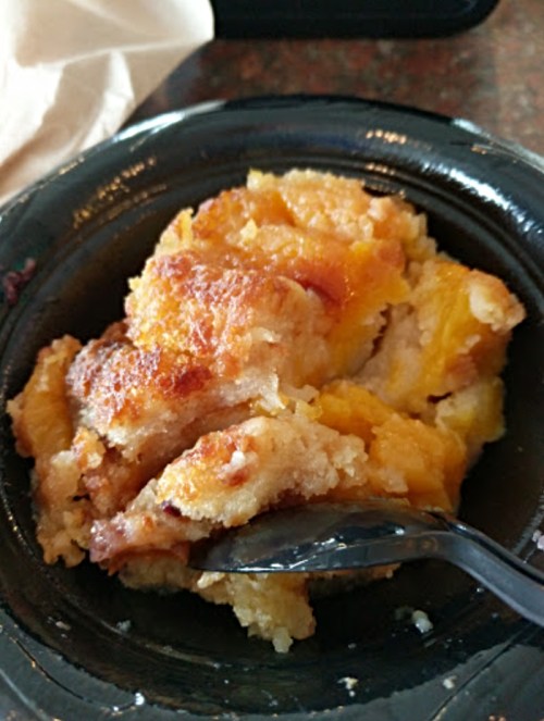 A serving of peach cobbler in a black bowl, with a fork resting on the side.