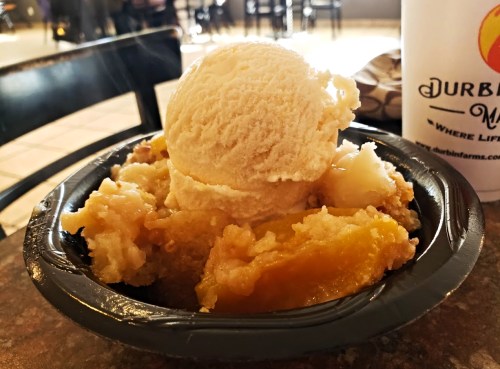A black bowl filled with warm peach cobbler topped with a scoop of vanilla ice cream.