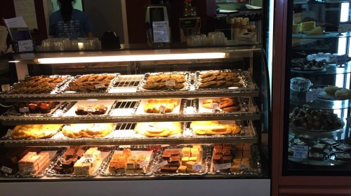 A display case filled with various baked goods, including cookies, pastries, and desserts, in a cozy café setting.