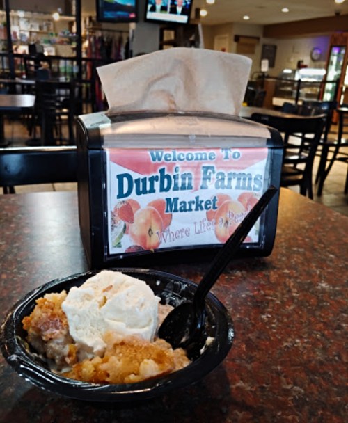 A bowl of dessert with ice cream sits on a table next to a sign for Durbin Farms Market.