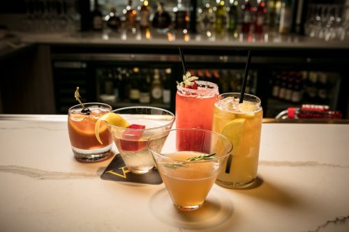 A variety of colorful cocktails on a bar counter, featuring garnishes and different glass styles.