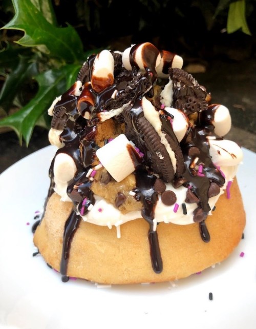 A decadent dessert featuring a cake topped with chocolate sauce, marshmallows, Oreos, and colorful sprinkles.