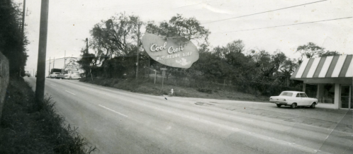 Black and white photo of a roadside scene featuring a large sign for "Cool Cove" and a vintage car parked nearby.