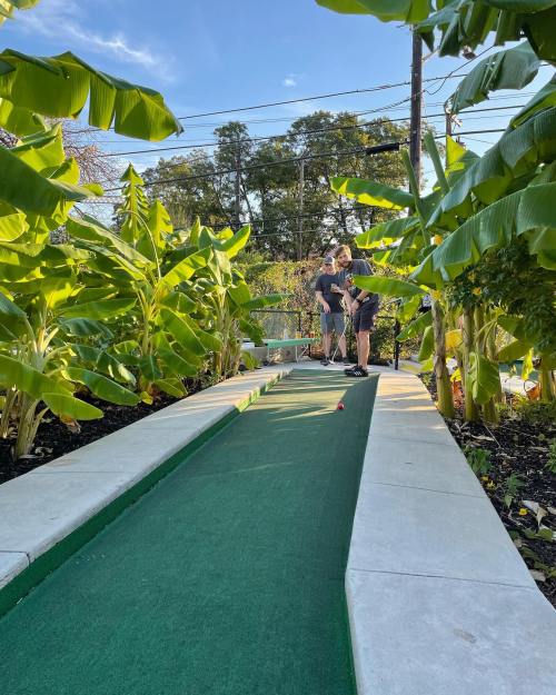 A mini-golf course surrounded by lush greenery, with two people preparing to take their shots.