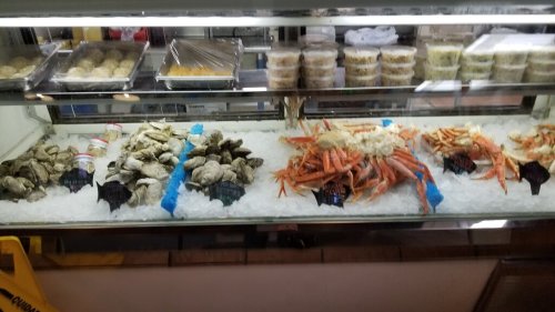 A seafood display featuring oysters, crabs, and other shellfish on ice, with labels and containers in the background.