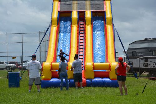 A colorful inflatable slide with people watching and enjoying a sunny day at an outdoor event.